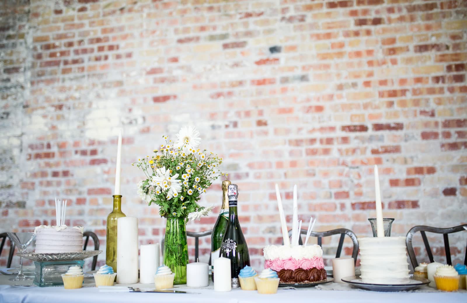 Baby shower dessert table with tiered cakes and candles against an exposed brick wall at The Venue at Redan II