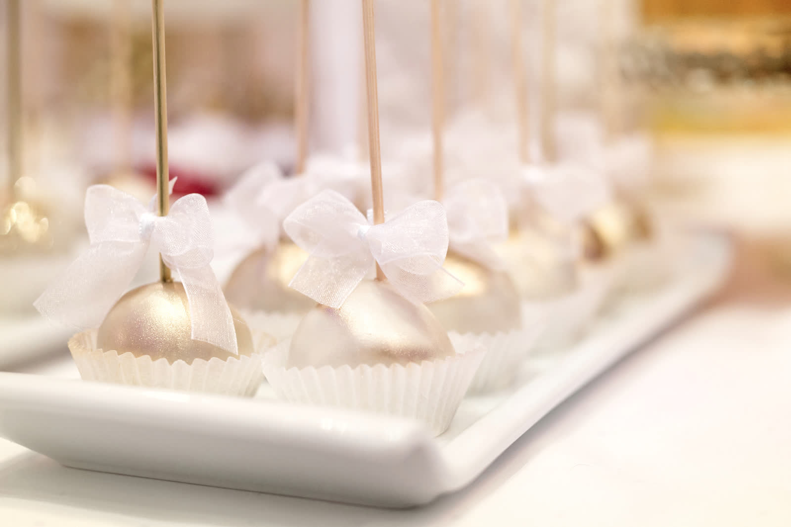 Pearlescent gold cake pops tied with white organza bows on a dessert tray at a Stone Mountain wedding reception