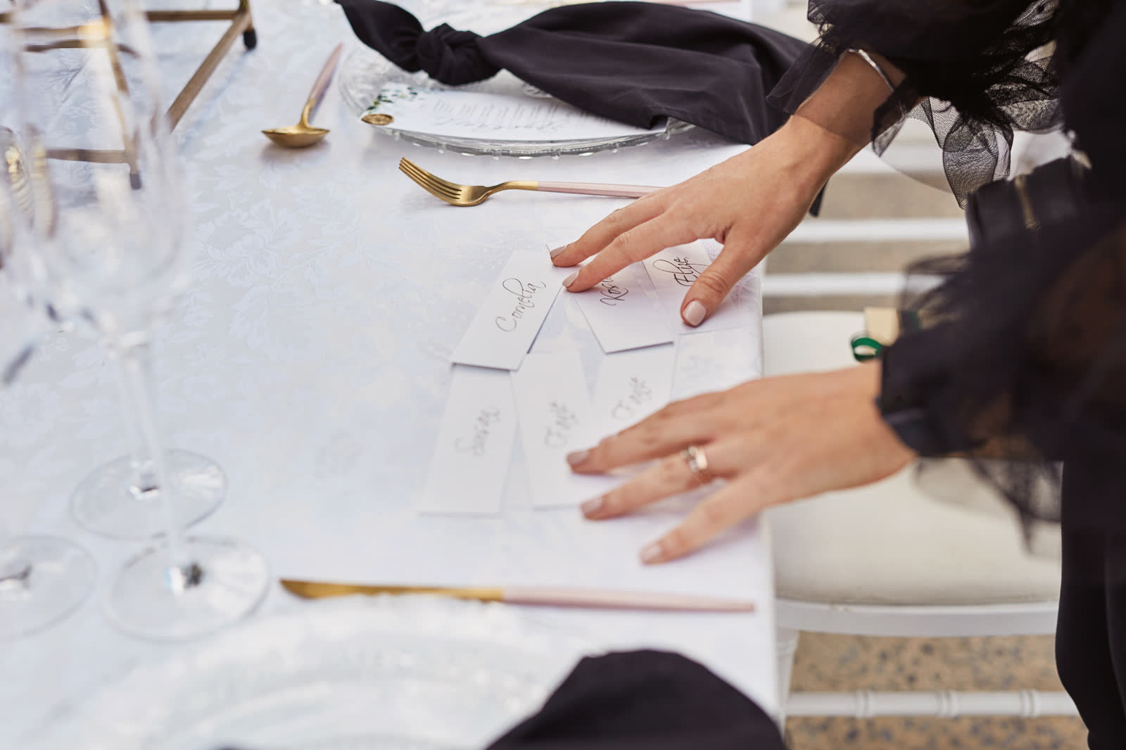 Hands arranging handwritten guest place cards on a damask linen runner at The Venue at Redan II